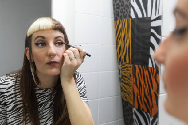 Frau trägt Eyeliner vor dem Badezimmerspiegel auf. Lässiger Look, Piercings und gefärbte Haare. Zebra- und Tigermuster Frau trägt Eyeliner vor dem Badezimmerspiegel auf. Lässiger Look, Piercings und gefärbte Haare. Stockbilder, lizenzfreie Fotos und Bilder mit Zebra- und Tigerdruck-Augen-Make-up