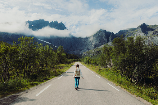 Rear view of female with long hair feeling happiness and running at the empty road with scenic view of the mountain range on Lofoten, Northern Norway