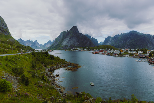 Panoramic photo of scenic village with old fisherman houses surrounded by the ocean and dramatic mountain peaks during cloudy summer day on Lofoten, Northern Norway