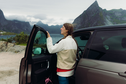 Side view of a woman with long hair enjoying a scenic view of the Nordic landscape from the car duting journey on Lofoten, Nordland county, Norway