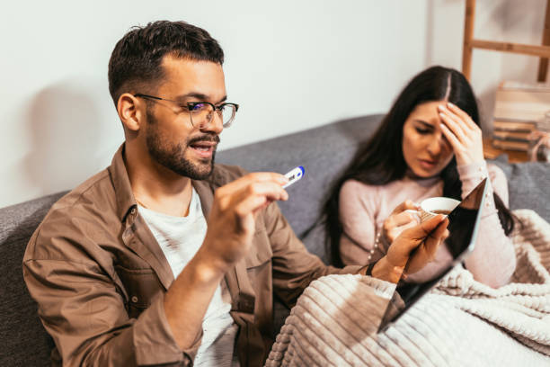 istock Young ill couple measuring temperature using thermometer at home. 1463472833