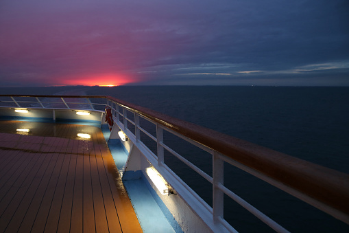 Beautiful final moments of the sunset with pink clouds over a cruise ship deck; a relaxing way to travel, sailing across the calm ocean.