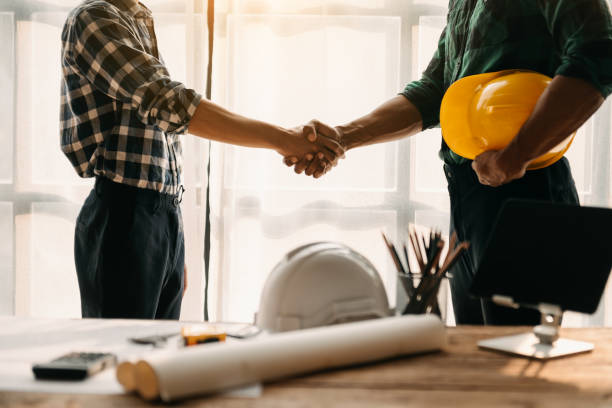 istock Construction team shake hands greeting start new project plan behind yellow helmet on desk in office center to consults about their building project. 1463477116