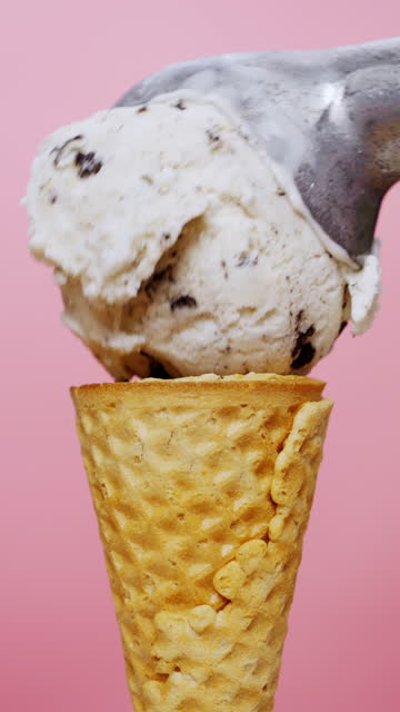 Vertical slow motion video, Scooping cookies and cream ice cream in a cone on pink background.