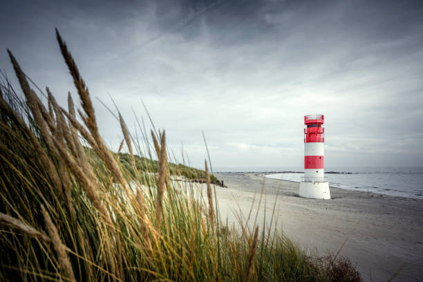Egmond aan Zee, Netherlands  August 31, 2024 - The approx. 28 m high white lighthouse and a woman sculpture with a view over the sea to the sailors who often do not return home, on a staircase in the sand dunes