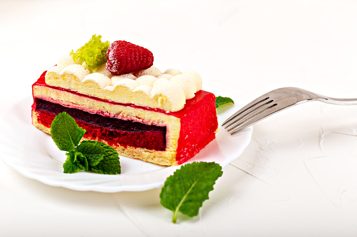 A piece of raspberry sponge cake with fluffy cream, mint and a fork on a white plate