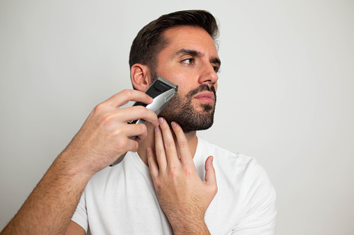 Handsome bearded man trimming his beard with a trimmer