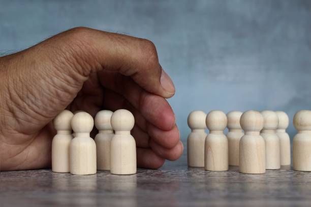 Hand separate group of wooden dolls Hand separate group of wooden dolls. Mass layoffs, downsizing concept. exclusion group of people separation fish out of water stock pictures, royalty-free photos & images