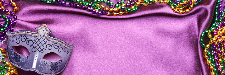Mardi Gras mask and beads on a purple satin background.
