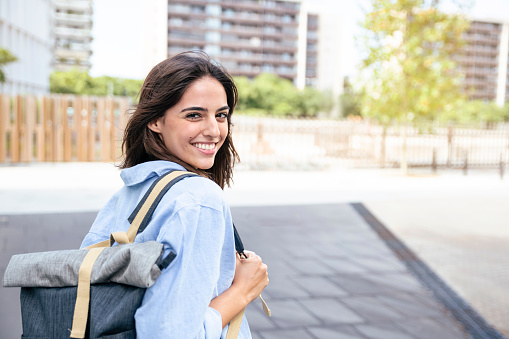Happy student with backpack in the campus. Portrait of smiling woman looking at camera with bakcpack. Education concept.