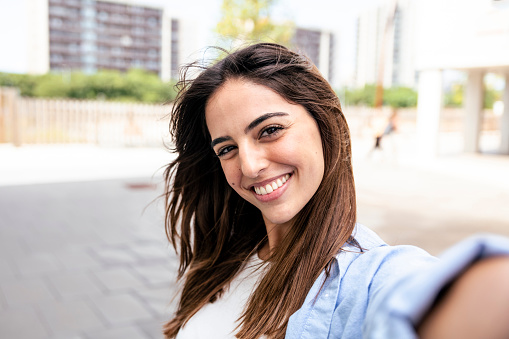 Selfie-portrait of pretty girl in the city. Portarit of happy young beautiful woman doing a selfie photo on the camera.