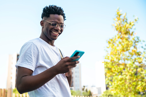 Happy young man smiling and looking his smartphone with a backpack in the park - Portrait of a handsome young man - education concept. High quality photo