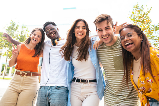 Low angle view of a happy group of multiracial friends looking at camera, enjoying outdoors. Multiethnic cheerful young people. High quality photo