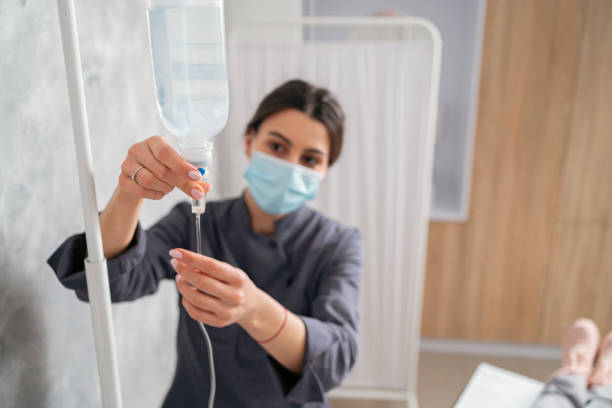 Female nurse adjusting IV drip At the medical clinic, Caucasian female nurse adjusting the infusion/IV on a senior female patient while she lying on the examination table alternative therapy stock pictures, royalty-free photos & images