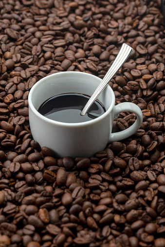 cup of black coffee with spoon in a background of coffee beans