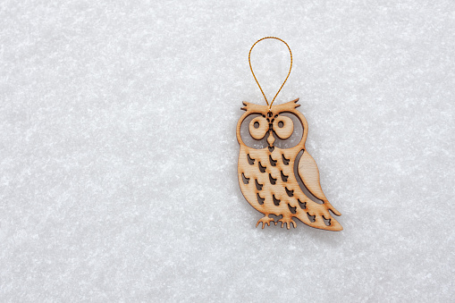 A Christmas tree toy in the form of a wooden owl lies on the snow