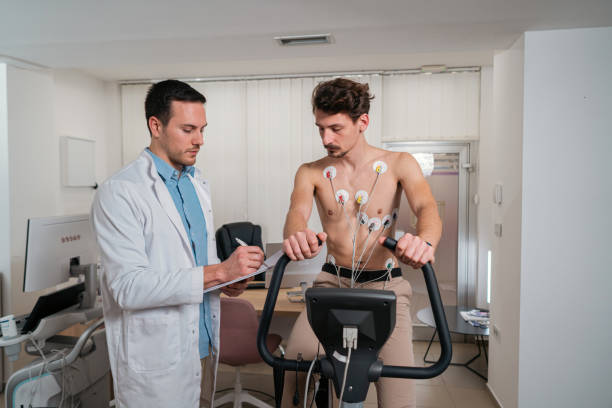 istock Male patient with electrodes on his chest, doing stress test on an exercise bicycle, while doctor observing him 1463493934
