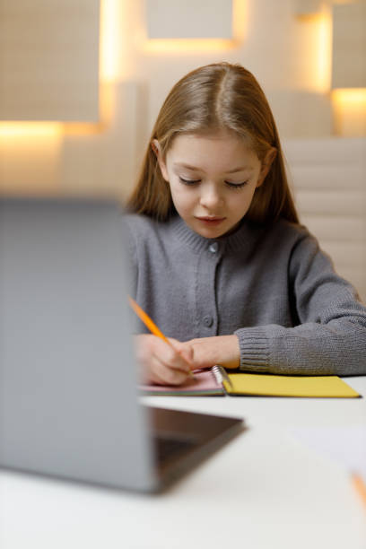 istock Remote learning, little girl writes lessons with a laptop, vertically. 1463494275