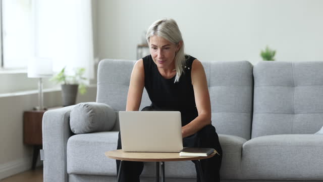 Thoughtful mature woman working on laptop at home