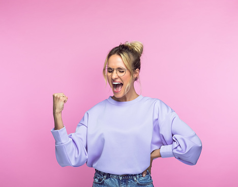Ecstatic mid adult woman screaming with clenched fist against pink background