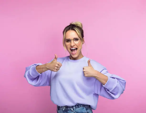 Portrait of happy mid adult woman gesturing thumbs up while standing against pink background