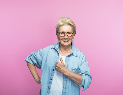 Portrait of happy senior woman showing thumbs up against pink background