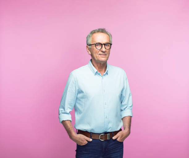 Confident senior man with hands in pockets Portrait of confident retired senior man standing with hands in pockets over pink background rolled up sleeves stock pictures, royalty-free photos & images