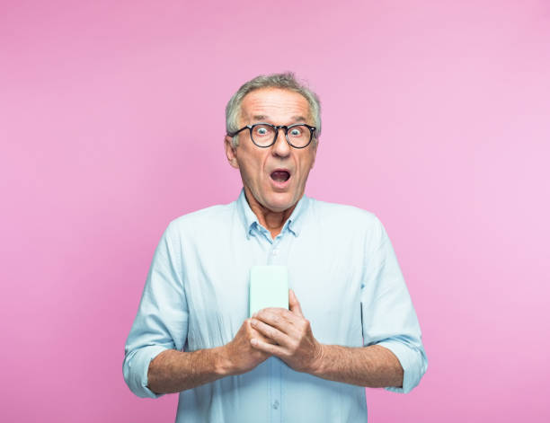 istock Shocked elderly man with mouth open holding phone 1463500155