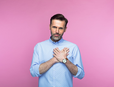 Portrait of man keeping hands on heart while standing against pink background