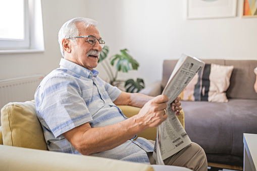 senior man with bad eyesight reading newspaper at home closeup