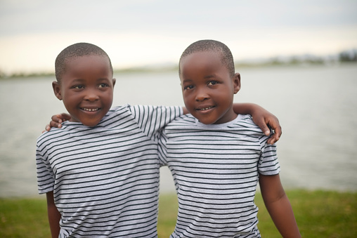 Hug, nature and twin boy children standing by the lake while on a summer vacation or weekend trip. Happy, smile and African kid brothers embracing outdoor with love, care and friendship on a holiday.