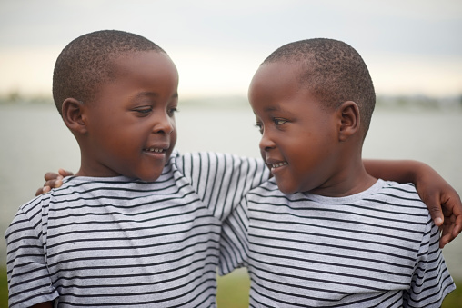 Happy, nature and boy twins hugging for love, care and friendship while on a summer vacation. Happiness, excited and African children embracing outdoor by the lake while on a holiday or weekend trip.