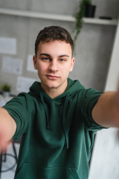 one man teenager stand in room at home wear green hoodie UGC selfie stock photo