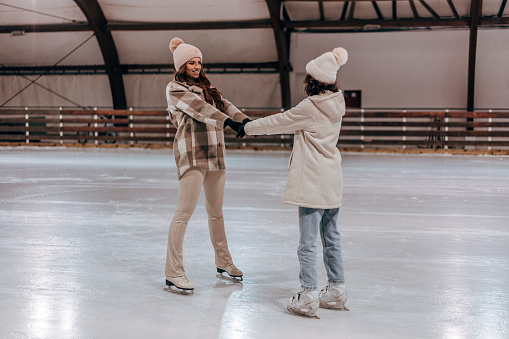 Two young women friends ice skating together in an ice rink, holding hands and having fun together
