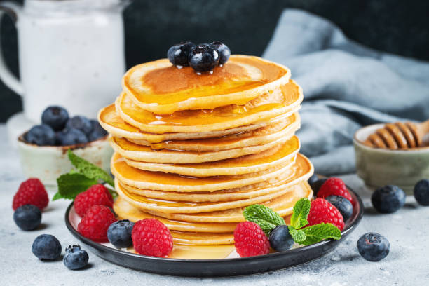 istock Delicious pancakes, with fresh blueberries, raspberry and maple syrup or honey on a dark background 1463511250