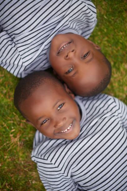 Smile, carefree and portrait of boys on grass for playing, bonding and relax in nature of Morocco. Happy, playful and face of African twins on a field in the countryside for sunshine and happiness stock photo
