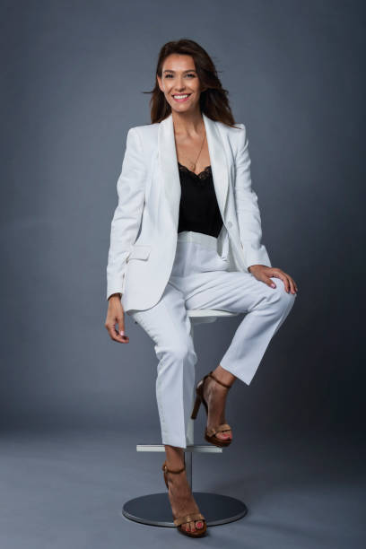 istock Smiling mid aged brunette woman sitting on a stool on isolated gray background 1463517516