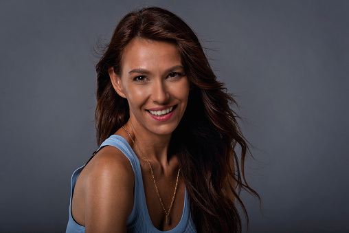 Close-up of brunette haired woman laughing and smiling against at grey background. Attractive female looking at camera.