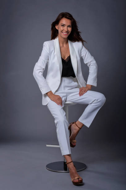 istock Smiling mid aged brunette woman sitting on a stool on isolated gray background 1463517582
