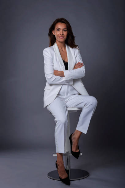 istock Smiling mid aged brunette woman sitting on a stool on isolated gray background 1463517611