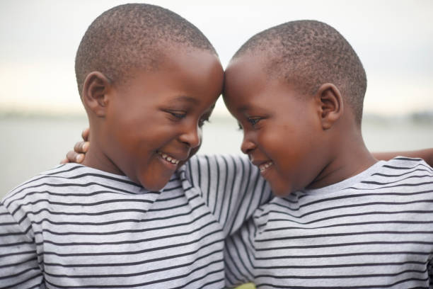 Love, bond and boy twins hugging for brotherhood, care and friendship while on summer vacation. Happiness, excited and African children embracing outdoor by the lake while on holiday or weekend trip. stock photo