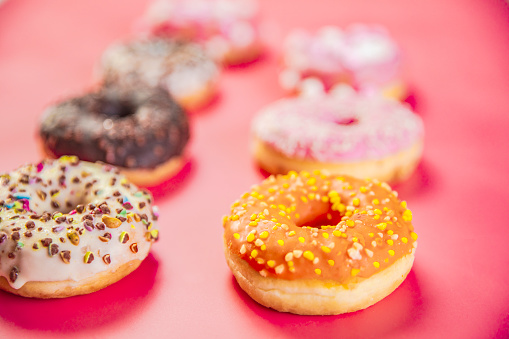 Doughnuts with multicolored glaze laid out in two rows on trendy pink background. Doughnuts are traditional sweet pastries. Copy space for text. top view