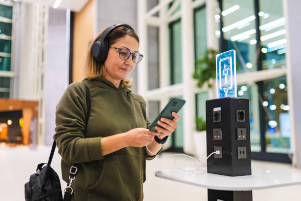 mujer esperando su vuelo en el aeropuerto mientras carga su teléfono en la estación de carga - information symbol audio fotografías e imágenes de stock