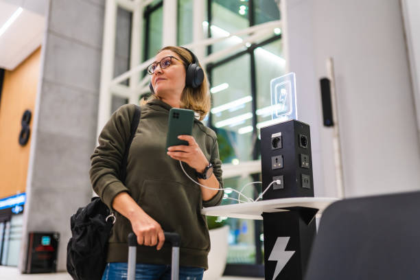 mujer esperando su vuelo en el aeropuerto mientras carga su teléfono en la estación de carga - information symbol audio fotografías e imágenes de stock