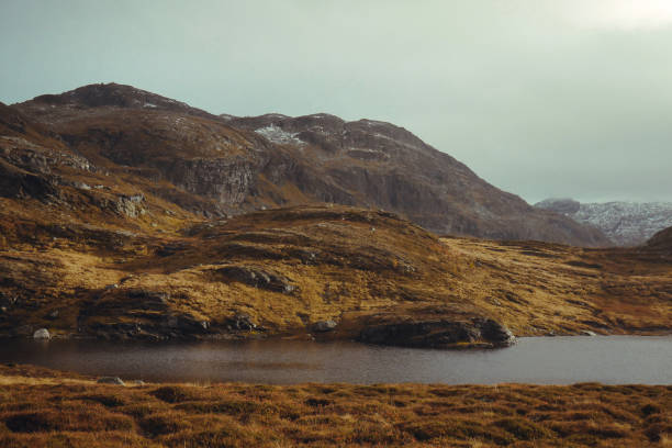 This lake sits in the sun in front of magnificent grass covered mountains. In the background, the clouds and snow rolls in.