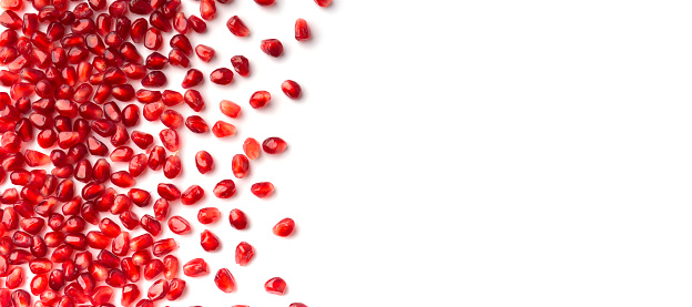 Red grains of a ripe pomegranate are neatly laid out on a white background top view. Pomegranate grains on isolated flat lay. Background of pomegranate seeds.