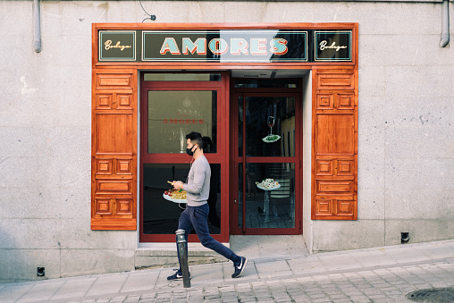 Madrid, Spain - October 10, 2020: Asian man walking down the street in front of a traditional restaurant in the trendy neighborhood of Lavapies.