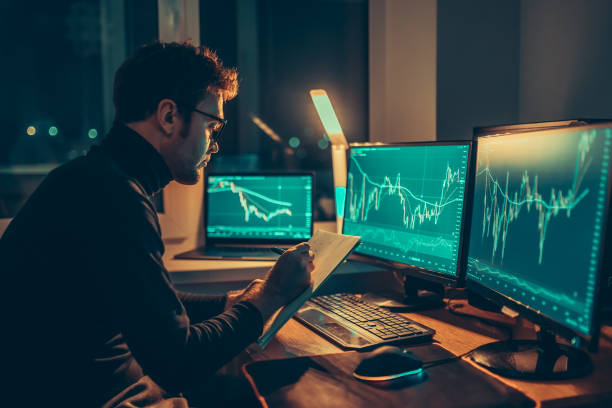 The Night Owl Trader Working late into the night, a man is seen from behind The Night Owl Trader Working late into the night, a man is seen from behind as he analyzes market trends and exchange information in his home office. multiscreen stock pictures, royalty-free photos & images