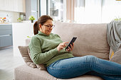Relaxed smiling woman sitting on sofa using phone
