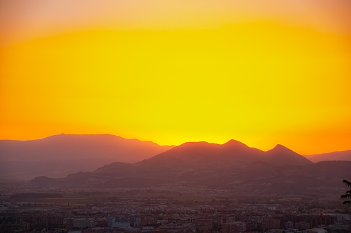 A beautiful orange sunset over a mountain range and town in Granada, Spain